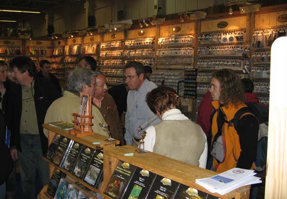 Le Stand Mouche de Charette. Au centre Jean-Marc Chignard,; responsable de la marque, et juste à sa gauche monsieurs Parrachini, organisateur de cet événement. En premier plan nous distinguons les vidéos de la marque, avec des sujets sur la mer comme la pêche du bar à la mouche en Bretagne.
